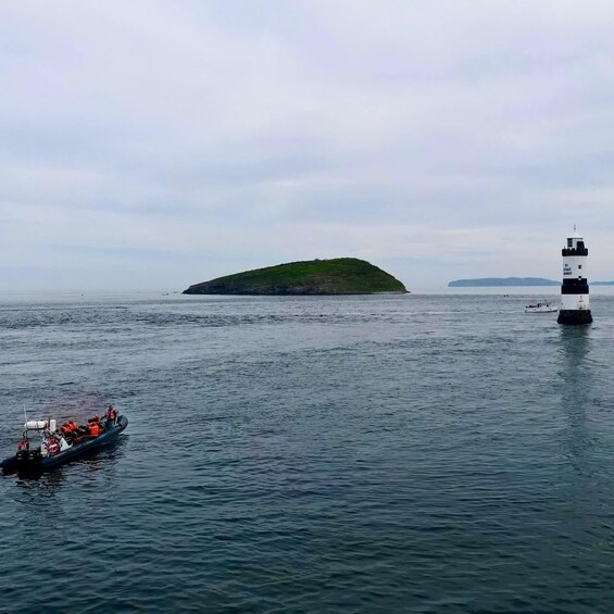 A boat with people wearing life jackets near a lighthouse and an island. 2