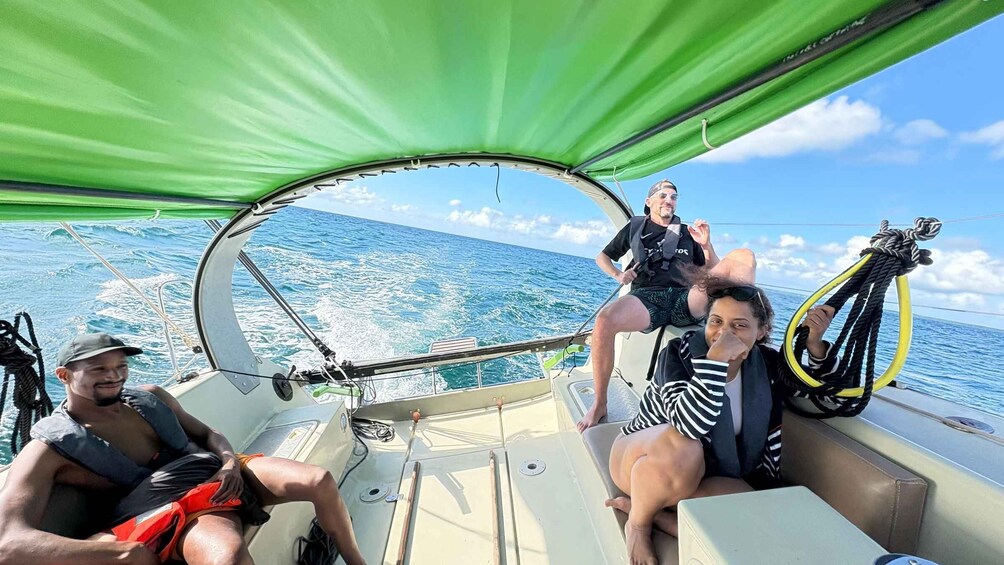 A sailboat with a green canopy, two people sitting, and one person standing. 3