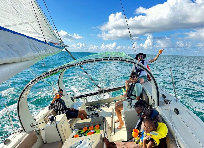 A sailboat with people on deck, including a child and an adult holding an orange drink. 1