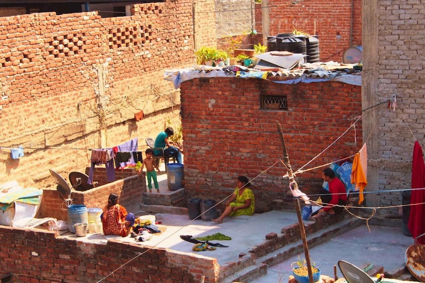 A courtyard with brick walls, a woman sitting, children playing, and laundry hanging. 4