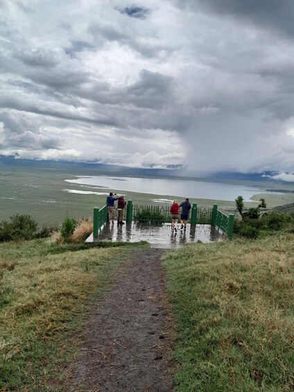 Un grupo de personas está de pie sobre un puente verde que cruza una zona inundada, bajo un cielo nublado. 5