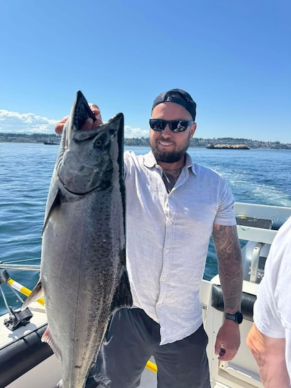 A person holding a large fish on a boat with a clear sky and water in the background. 4