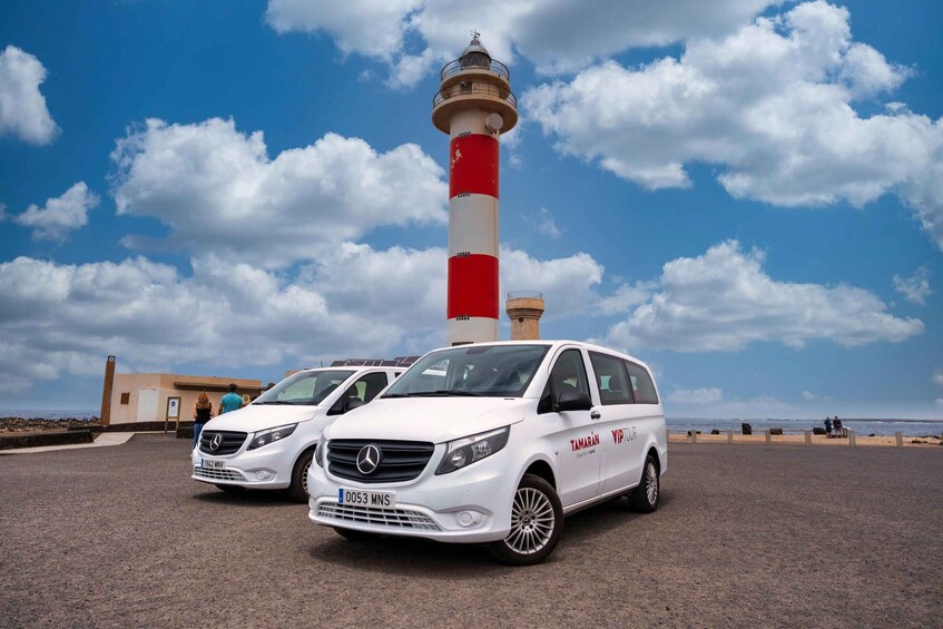 Two white Mercedes vans parked near a lighthouse. 2