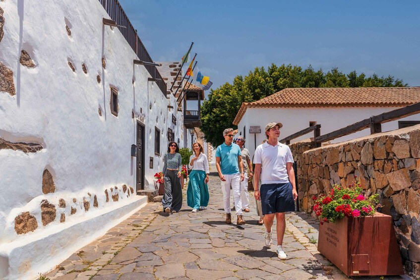 A narrow cobblestone street lined with white buildings, a stone wall, and a sign for a historical capital. 1
