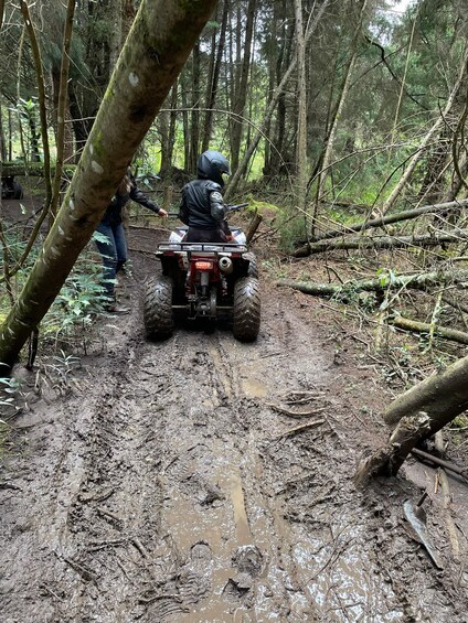 A person riding an ATV on a muddy trail in a forest. 1