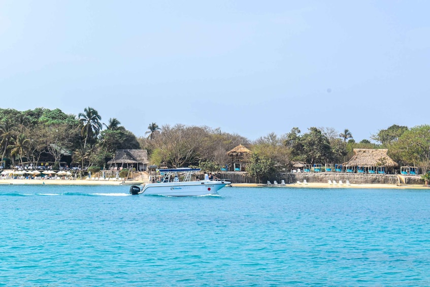 A boat on turquoise water with a beach and thatched-roof structures in the background. 3