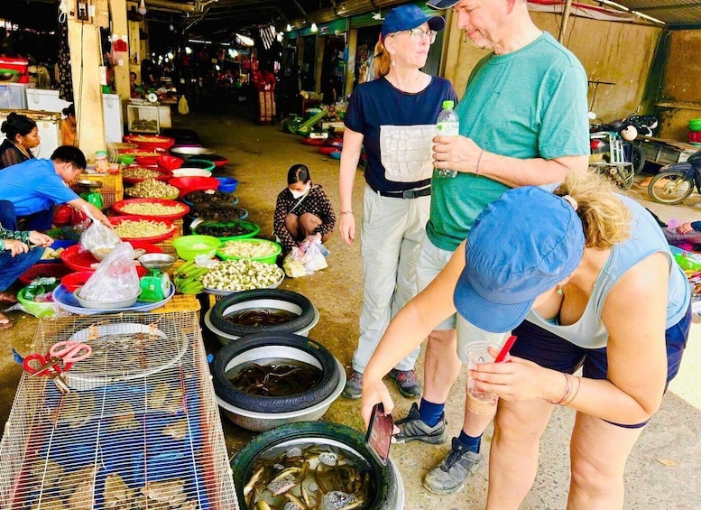 A market with people buying and selling goods, including fish in large bowls and various vegetables in baskets. 3