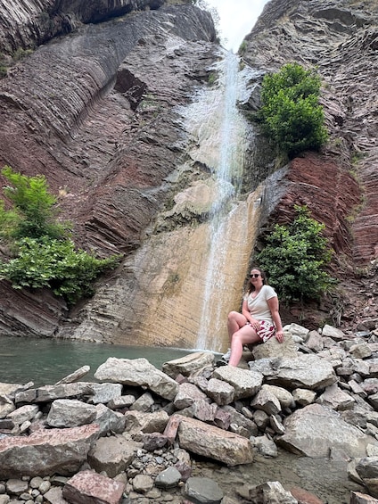 A waterfall cascading down a rocky cliff with a person sitting on rocks at the base. 4