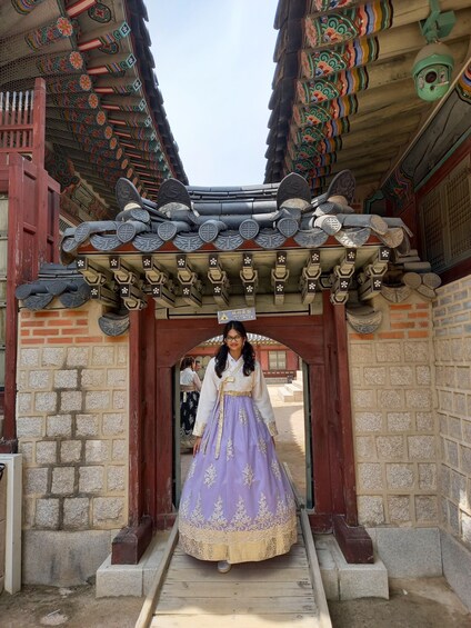 A traditional Korean gate with intricate roof decorations and a person in a hanbok. 4