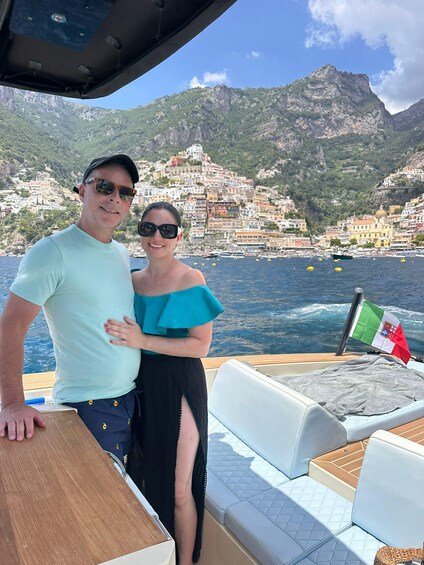 A couple on a boat with a coastal town and mountains in the background. 4