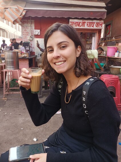 A person holding a glass of coffee in front of a shop with a sign in a local language. 1