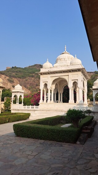 A white marble pavilion with domes and arches, surrounded by well-manicured gardens and hills in the background. 4