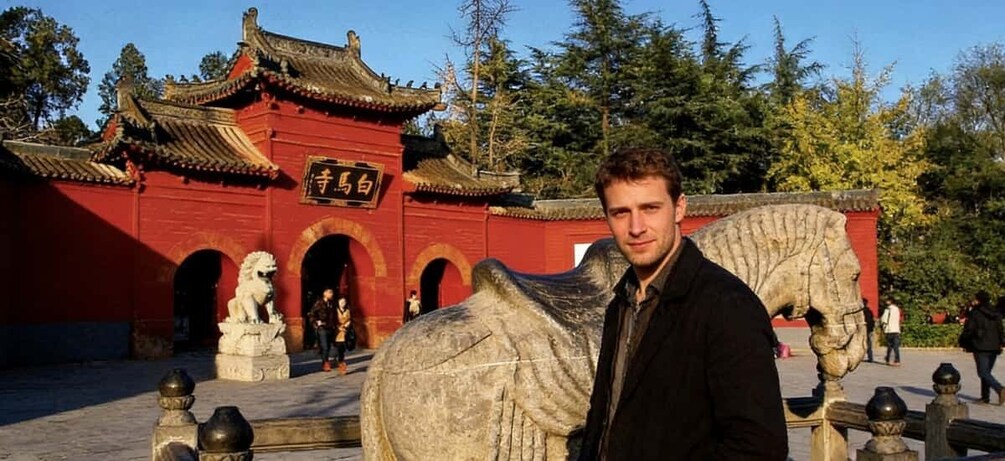 A man standing in front of a traditional Chinese building with a lion statue. 1