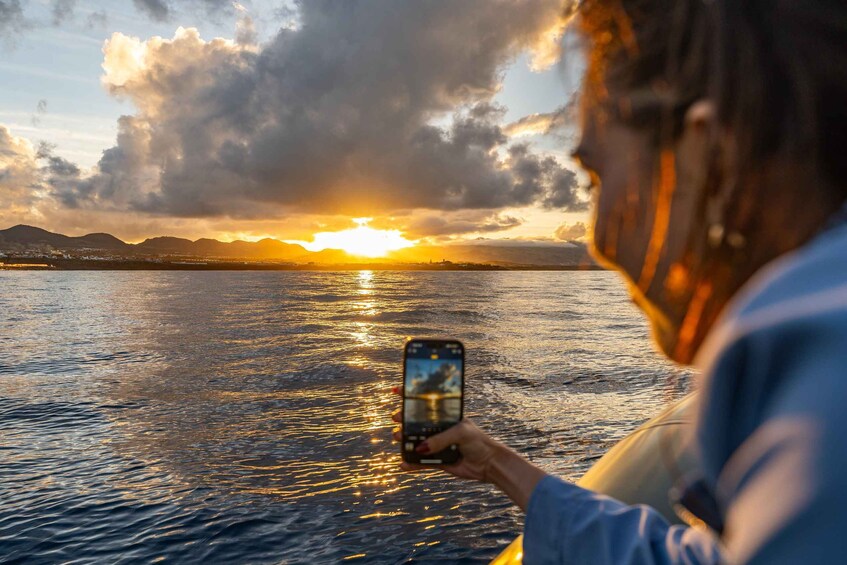 A person taking a photo of a sunset over water with mountains in the background. 5