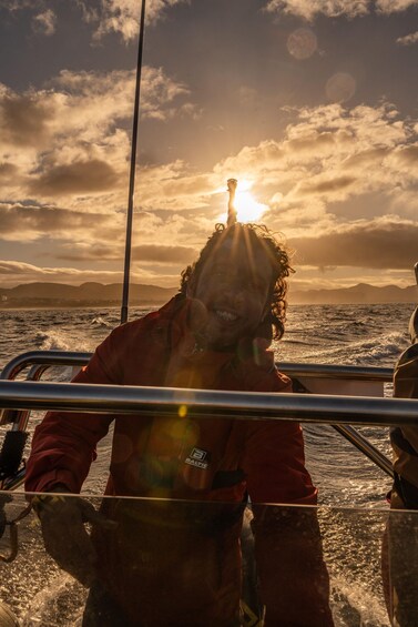 A person in a red jacket on a boat with the sun setting in the background. 3