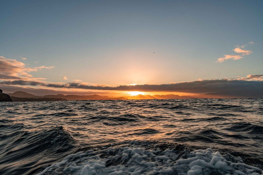 A sunset over a choppy sea with waves and distant mountains. 2