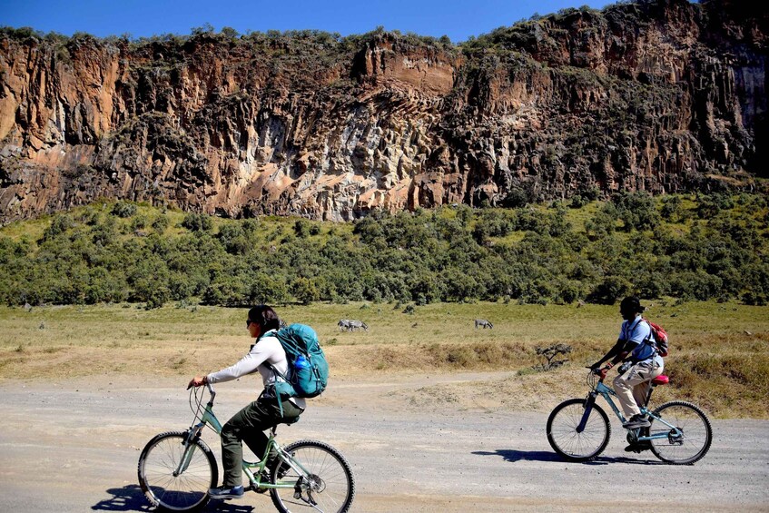 Two cyclists on a dirt path with a rocky cliff in the background. 2
