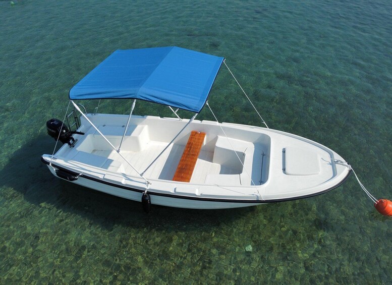 A small white motorboat with a blue canopy and an orange seat, anchored in clear shallow water. 1