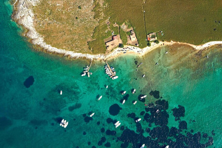 An aerial view of a coastal area with clear turquoise waters, boats anchored near the shore, and a small settlement with buildings and a road. 2