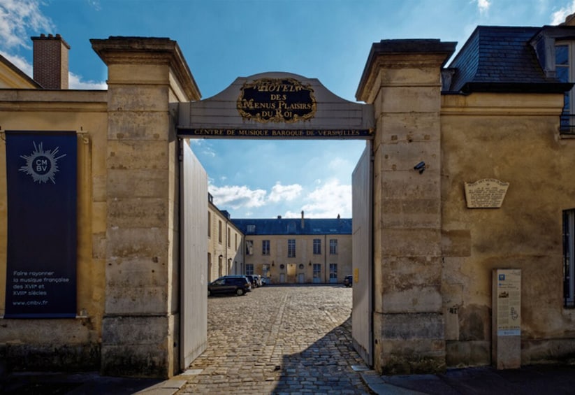 An entrance to a historic building with a sign reading 'HOTEL DES MENUS PLAISIRS DU ROI' and a plaque for 'CENTRE DE MUSIQUE BAROQUE DE VERSAILLES.' 2
