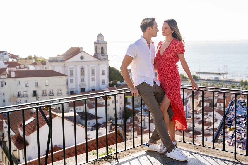 A couple on a balcony overlooking a cityscape with historic buildings and a view of the sea. 1