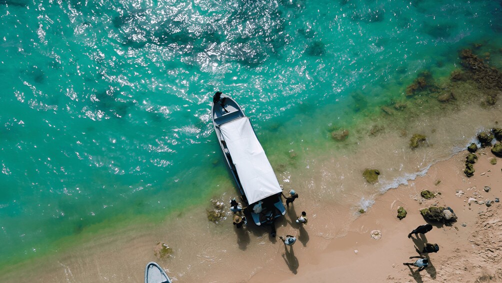 An aerial view of a boat anchored near a beach with clear turquoise water and rocky shoreline. 1