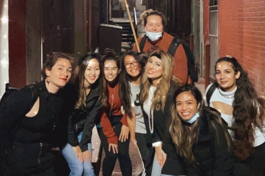 Un groupe de personnes posant dans une ruelle bordée de murs en briques et surmontée d’une grille métallique. 3