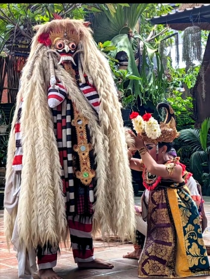 A person in a traditional costume with a large, ornate mask and a feathered headdress, standing in a garden with tropical plants. 5