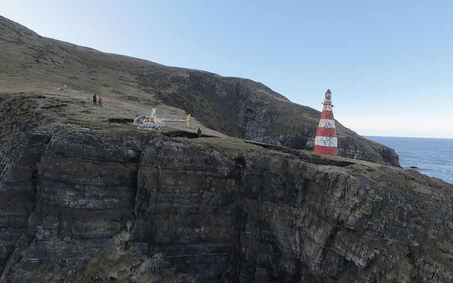 A rocky coastline with a lighthouse and a small aircraft on the cliff edge. 3