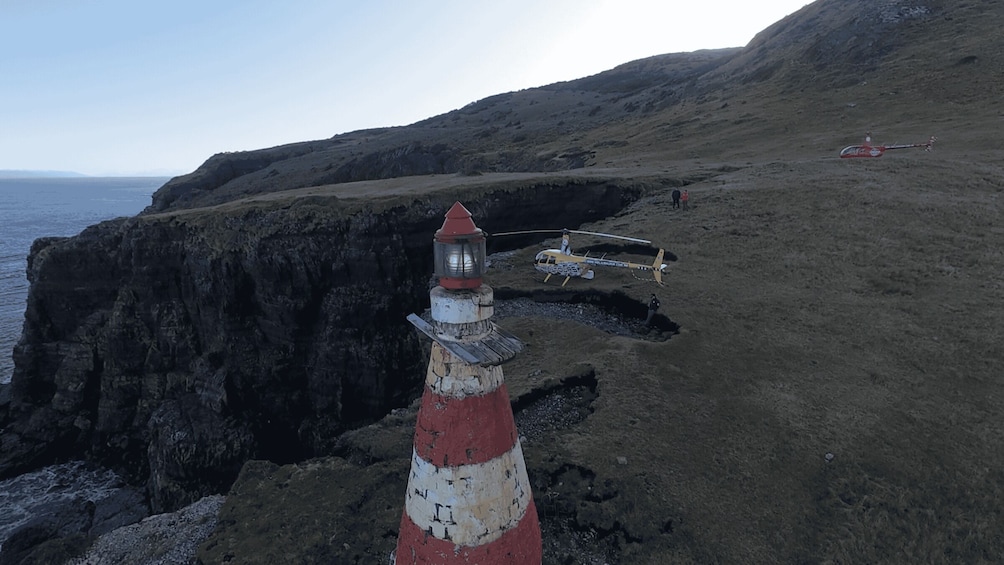A lighthouse on a rocky cliff with a helicopter in the background. 4