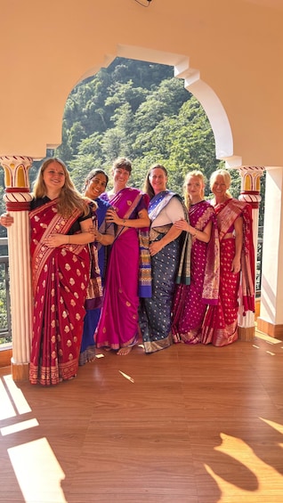 A group of people in traditional attire standing in a room with a view of a forested landscape. 1