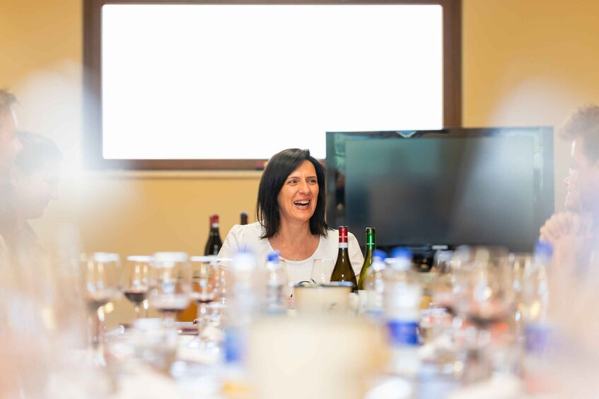 A conference room with a presentation screen, a table with wine bottles and glasses, and attendees seated around the table. 3