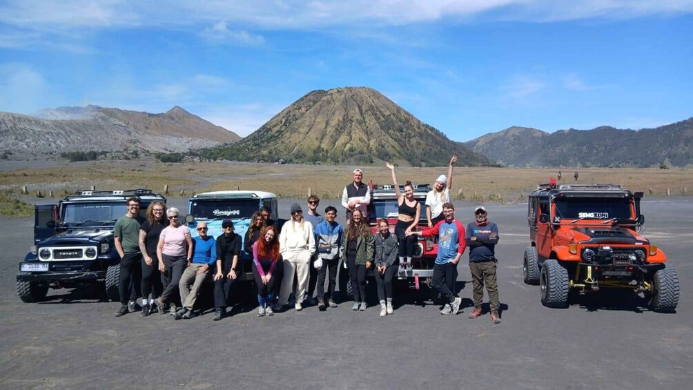 A group of people posing in front of a black Toyota Land Cruiser, a blue Mercedes-Benz G-Class SUV, and an orange Jeep Wrangler. 4
