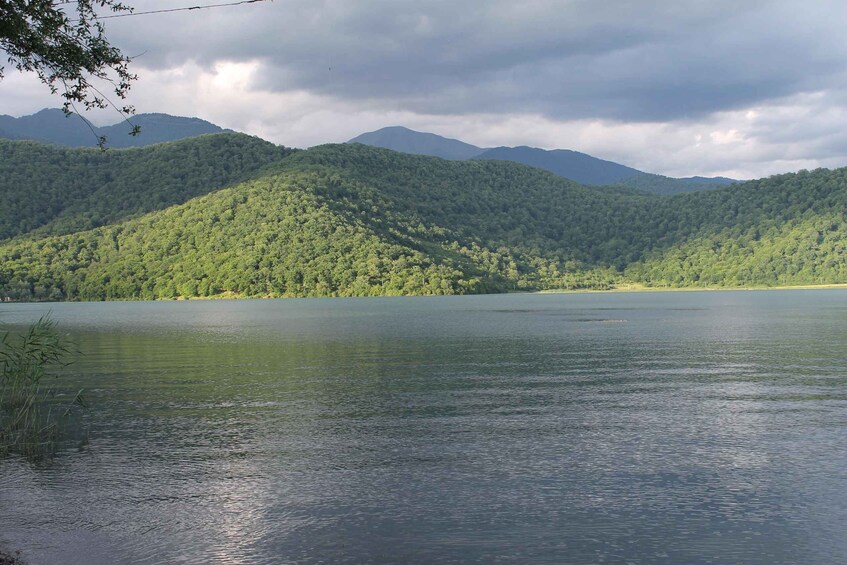 A calm lake surrounded by lush green hills under a cloudy sky. 3