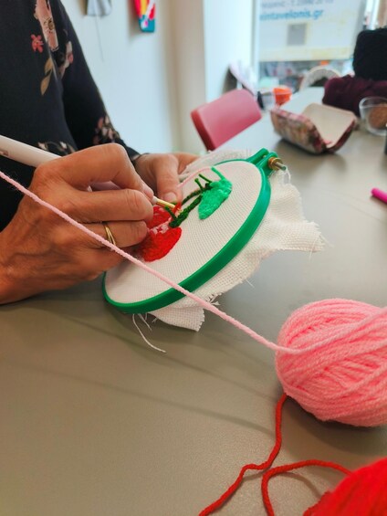 Iemand borduurt een ontwerp op stof, met behulp van een groene borduurnaald en roze en rode garen. 4