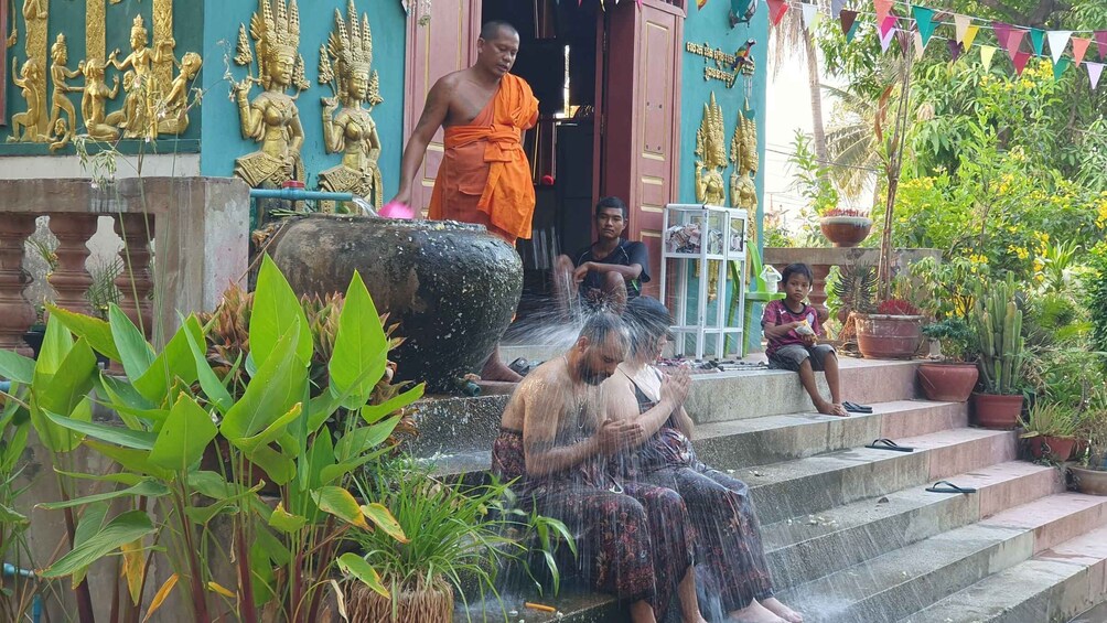 A temple entrance with golden statues, a monk, and people washing at a water fountain. 3