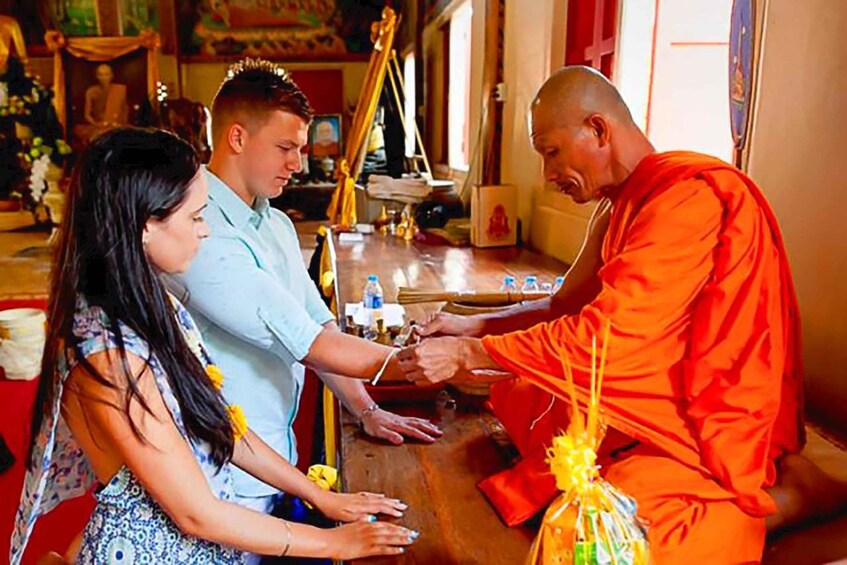A person in orange robes receiving offerings from two individuals. 5