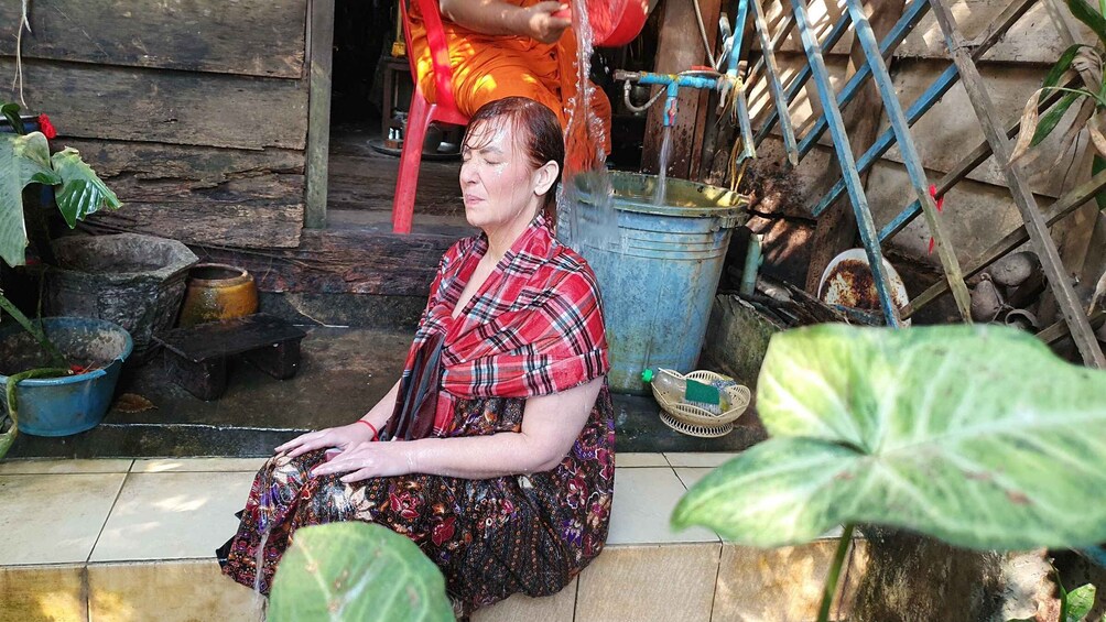 A woman sitting on a tiled floor in front of a rustic wooden structure. 2