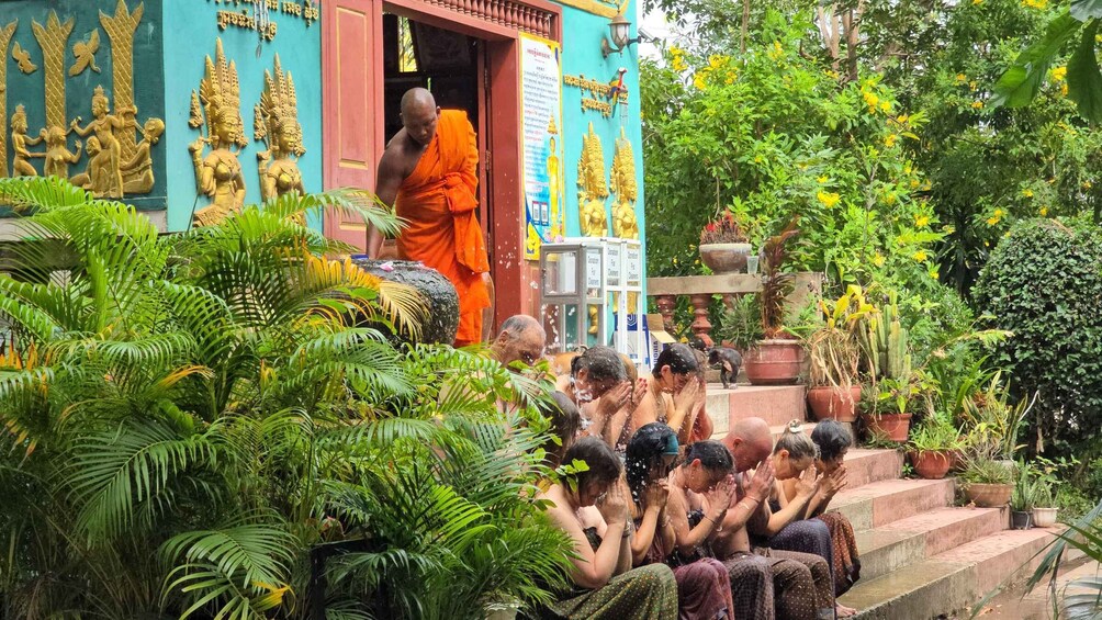 A temple with golden statues and a monk in orange robes. People are sitting on steps, some with their hands in prayer. 1