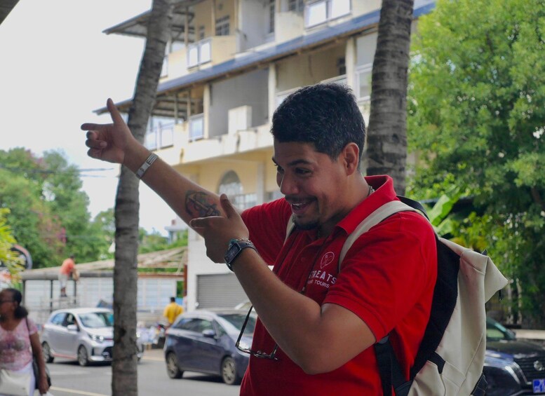 A person in a red shirt pointing to something off-camera, with a backpack and a watch visible. 3