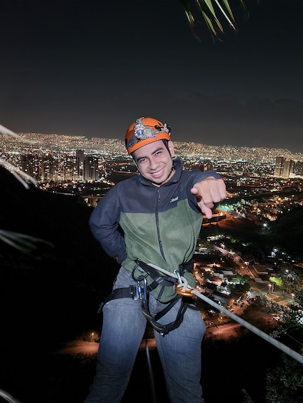 A person rappelling with a harness and helmet, overlooking a cityscape at night. 2