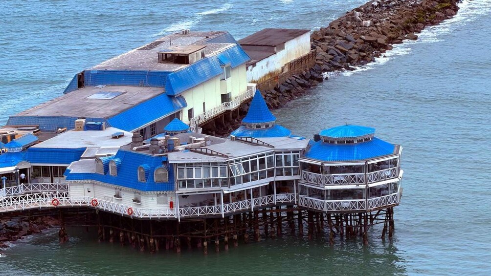 A floating structure with blue roofs and white walls, supported by pillars in the water. 2