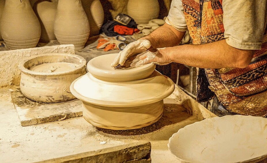 A person shaping a clay pot on a pottery wheel. 1