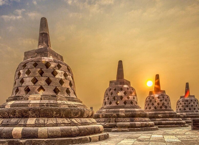 A row of stone stupas with a sun setting in the background. 3