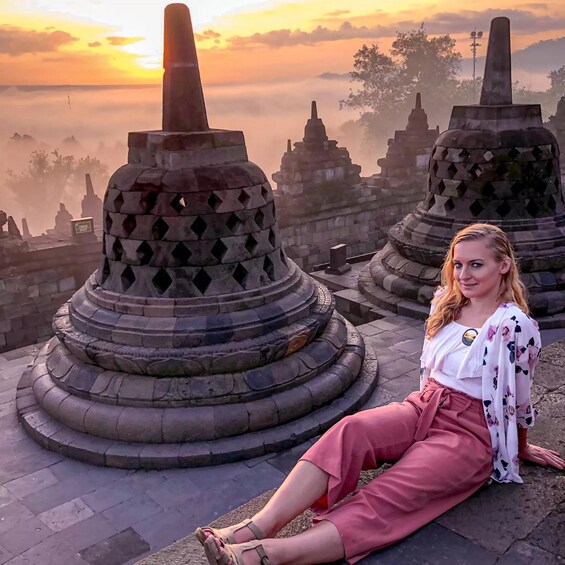 A person sitting on stone steps in front of ancient stone structures with a sunset in the background. 4
