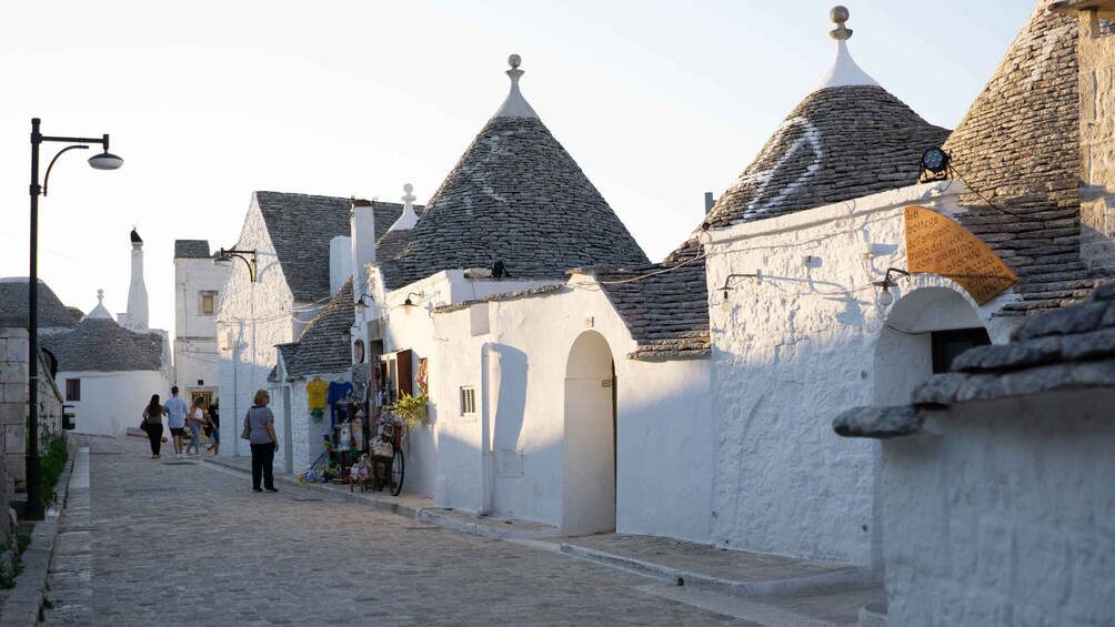 A narrow cobblestone street lined with white buildings with stone roofs. 5