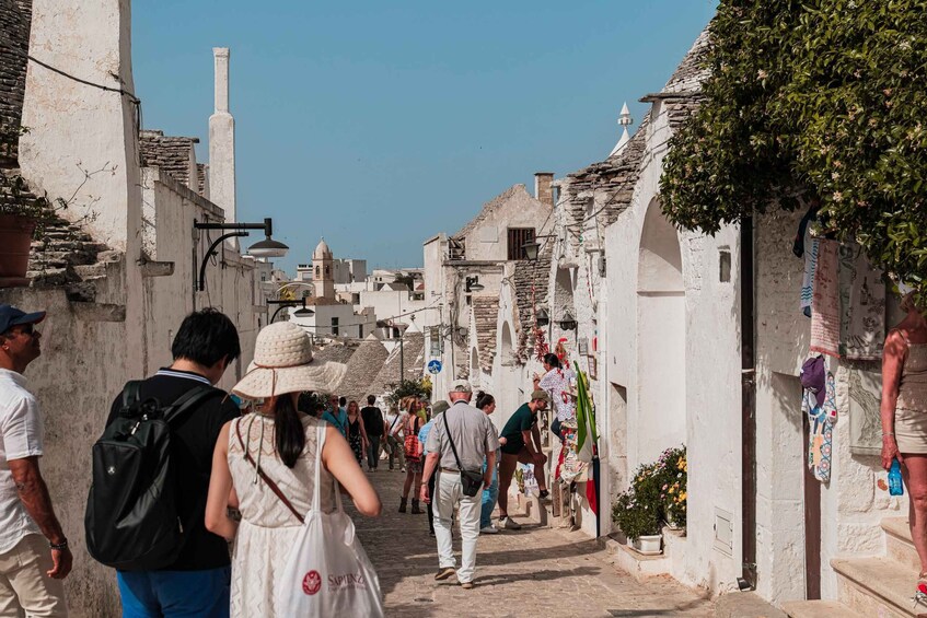 A narrow street lined with white buildings, some with arches and a bell tower in the distance. 4