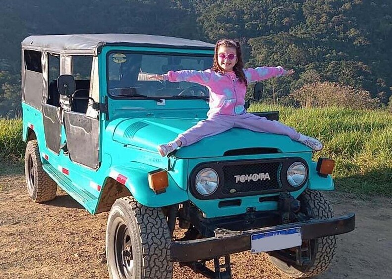 A turquoise Toyota off-road vehicle parked on a dirt path with a person sitting on the hood. 5