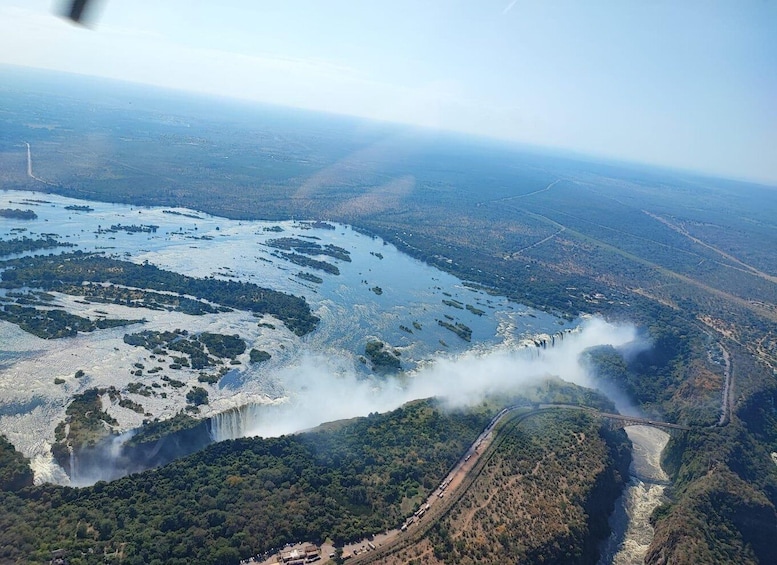 An aerial view of a river with a waterfall, surrounded by forested areas and a bridge. 5