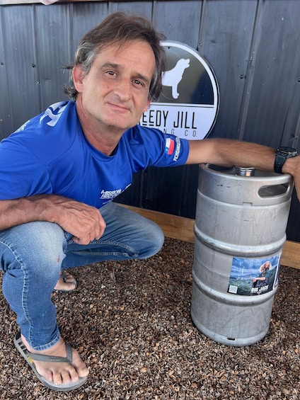 En man i blå skjorta och jeans hukar sig bredvid en silverfärgad tunna med en etikett på. 5